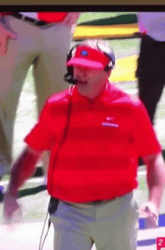 a man wearing a red shirt and a visor is standing on a football field