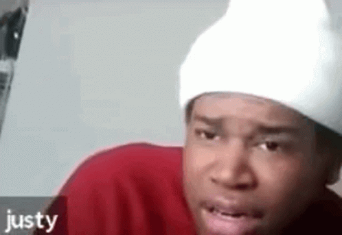 A Man Wearing A Red Shirt And A White Beanie Is Making A Funny Face . GIF