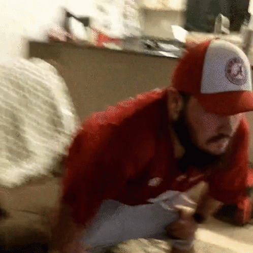 A Man Wearing A Red Shirt And A White Hat With A Logo On It Is Kneeling Down GIF