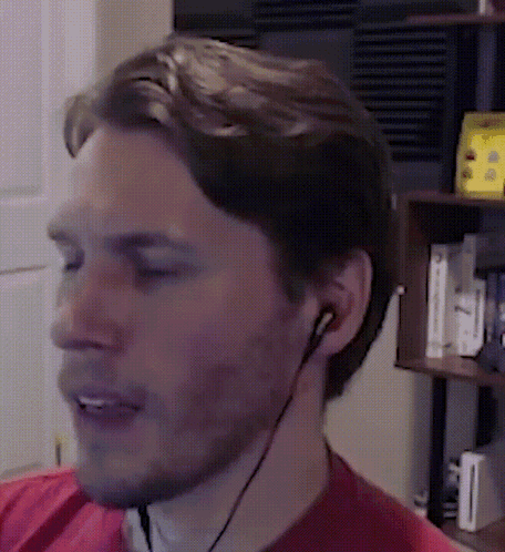 A Man Wearing A Red Shirt And Earbuds Looks At Something GIF