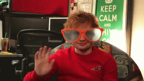A Man Wearing A Red Shirt And Orange Glasses Is Waving In Front Of A Keep Calm Sign GIF