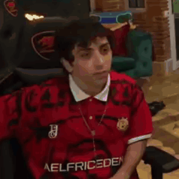 A Man Wearing A Red Shirt Is Sitting In A Chair . GIF