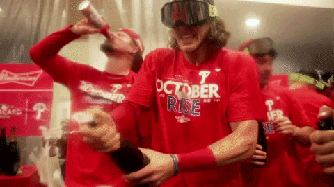 A Man Wearing A Red Shirt That Says October Rise Is Drinking A Beer GIF