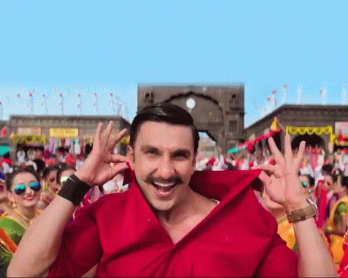 A Man Wearing A Red Shirt With A Mustache Is Smiling In Front Of A Crowd GIF