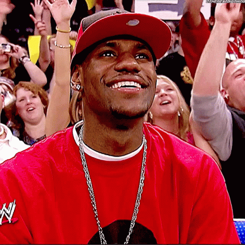 A Man Wearing A Red Shirt With The Word N On It Smiles In Front Of A Crowd GIF