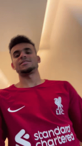 A Man Wearing A Red Shirt With The Word Standard Chartered On It GIF