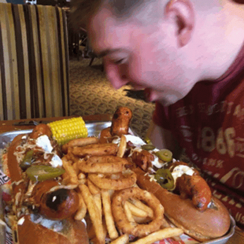 A Man Wearing A Red Shirt With The Year 1886 On It Is Eating A Hot Dog GIF