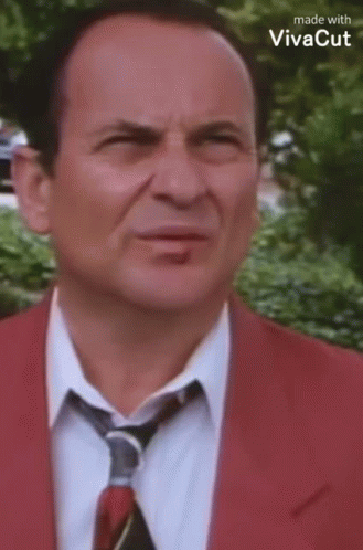 A Man Wearing A Red Suit And Tie Is Making A Funny Face . GIF