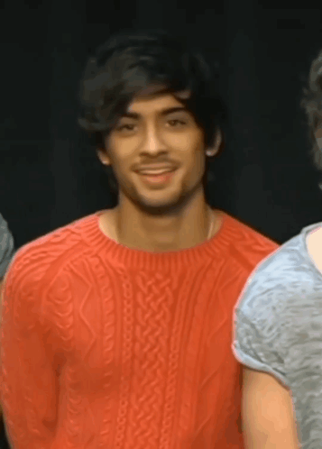 A Man Wearing A Red Sweater Is Smiling And Looking At The Camera GIF
