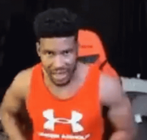A Man Wearing A Red Under Armour Tank Top Is Smiling And Looking At The Camera . GIF