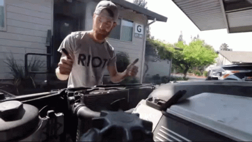 A Man Wearing A Riot T-Shirt Is Working On A Car GIF