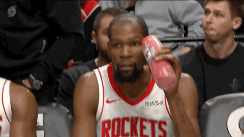 A Man Wearing A Rockets Jersey Is Holding A Can Of Soda GIF