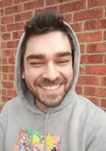 A Man Wearing A Rugrats Hoodie Smiles In Front Of A Red Brick Wall GIF