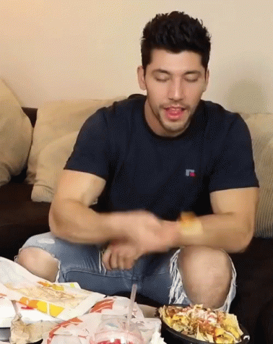 A Man Wearing A Russell T-Shirt Is Sitting On A Couch Eating Chips GIF
