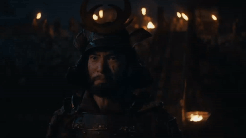 a man wearing a samurai helmet stands in the dark