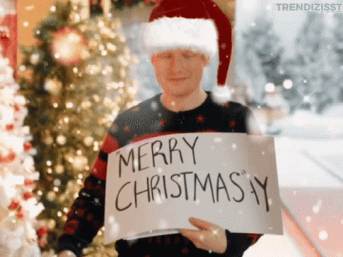 A Man Wearing A Santa Hat Holds A Sign That Says Merry Christmas GIF