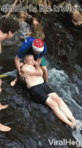 A Man Wearing A Santa Hat Is Helping Another Man In A Waterfall GIF
