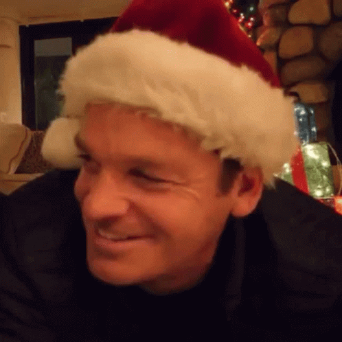 A Man Wearing A Santa Hat Is Smiling In A Living Room . GIF