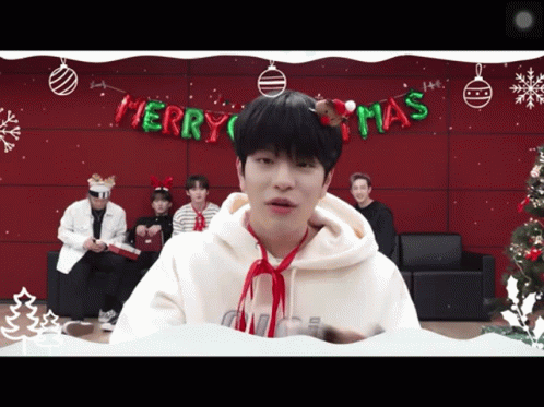 A Man Wearing A Santa Hat Stands In Front Of A Merry Christmas Banner GIF