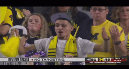 a man wearing a scarf and a michigan shirt stands in the crowd