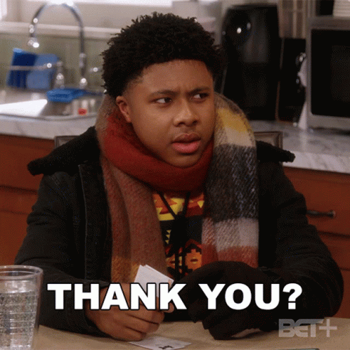 A Man Wearing A Scarf Is Sitting At A Table Holding A Piece Of Paper That Says Thank You GIF