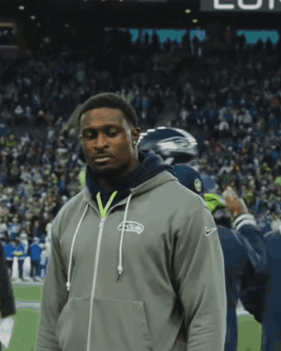 a man wearing a seahawks hoodie stands on a field
