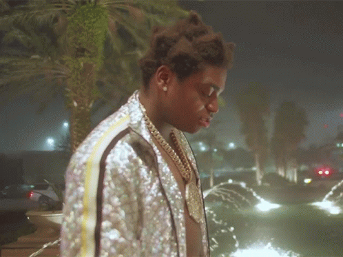 A Man Wearing A Sequined Jacket Stands In Front Of A Fountain GIF