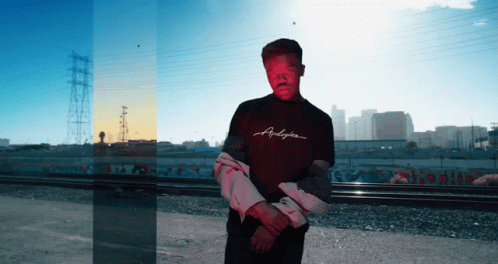 A Man Wearing A Shirt That Says Andyson Stands In Front Of A City GIF