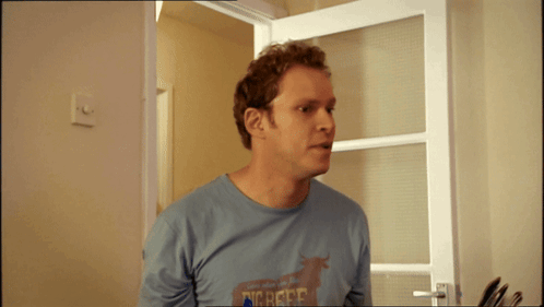 A Man Wearing A Shirt That Says Dig Here Is Standing In Front Of A Door GIF