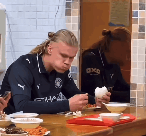 A Man Wearing A Shirt That Says Etihad Is Eating Food GIF