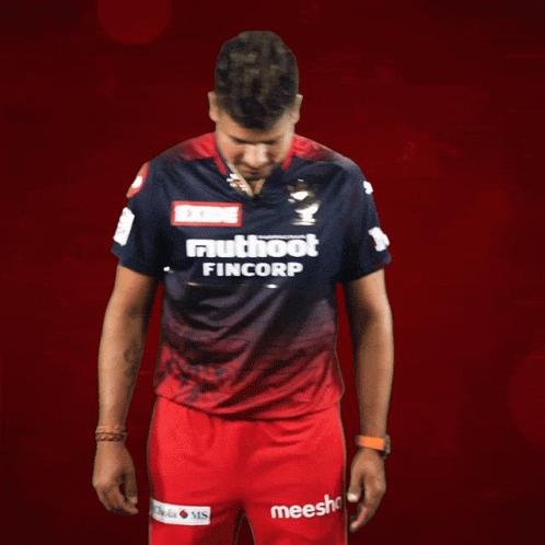 A Man Wearing A Shirt That Says Exide Muthoot Fincorp Stands In Front Of A Red Background GIF