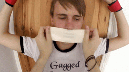 A Man Wearing A Shirt That Says " Gagged " Is Being Tickled GIF