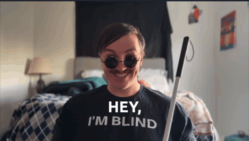 A Man Wearing A Shirt That Says Hey I 'M Blind Is Holding A Cane GIF