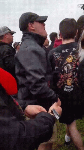 A Man Wearing A Shirt That Says Hot Rod Is Standing In A Crowd Of People GIF