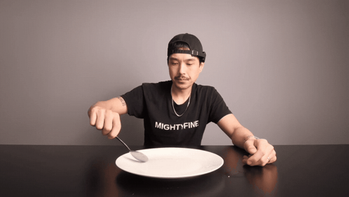 A Man Wearing A Shirt That Says Mightyfine Is Holding A Spoon Over A Plate GIF