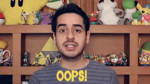 A Man Wearing A Shirt That Says Oops Is Standing In Front Of A Shelf Full Of Toys GIF