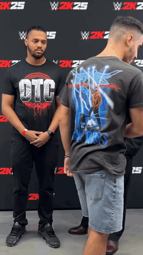 A Man Wearing A Shirt That Says Otg Stands Next To Another Man GIF