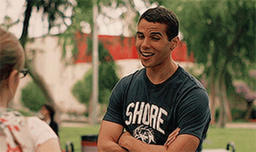 A Man Wearing A Shirt That Says Shore Is Talking To A Woman . GIF