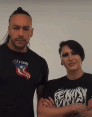 A Man Wearing A Shirt That Says Strong Stands Next To A Woman Wearing A Shirt That Says Ena GIF