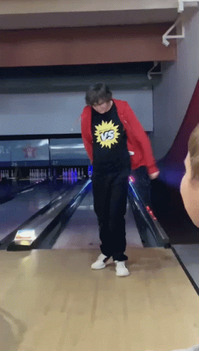 A Man Wearing A Shirt That Says Vs On It Stands On A Bowling Alley GIF