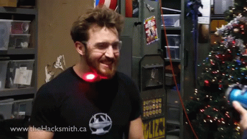 A Man Wearing A Shirt That Says Www.thehacksmith.ca Smiles In Front Of A Christmas Tree GIF