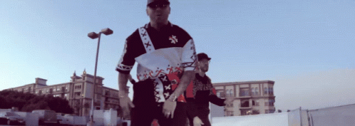 A Man Wearing A Shirt That Says Xxx On It Stands Next To Another Man GIF