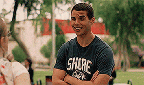 A Man Wearing A Shore T-Shirt Is Talking To A Woman In A Park . GIF