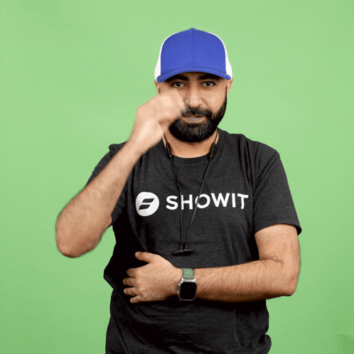 A Man Wearing A Showit Shirt Covers His Face With A Blue Hat GIF