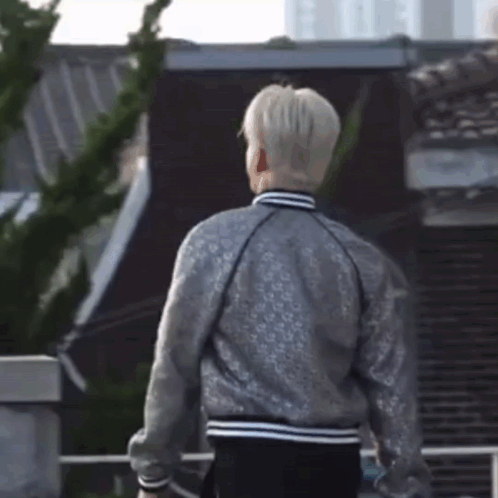A Man Wearing A Silver Jacket Is Standing In Front Of A Building GIF