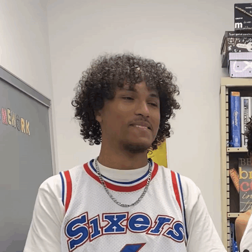 A Man Wearing A Sixers Jersey Stands In Front Of A Blackboard GIF