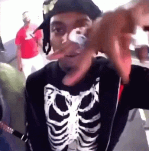 A Man Wearing A Skeleton Shirt And A Hat Is Making A Funny Face GIF