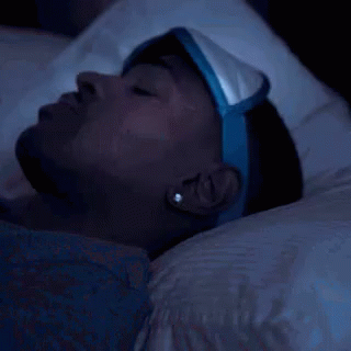 A Man Wearing A Sleep Mask Is Laying In Bed At Night . GIF