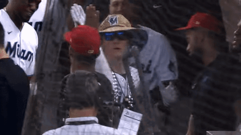 A Man Wearing A Straw Hat With The Letter M On It Is Surrounded By Miami Baseball Players GIF