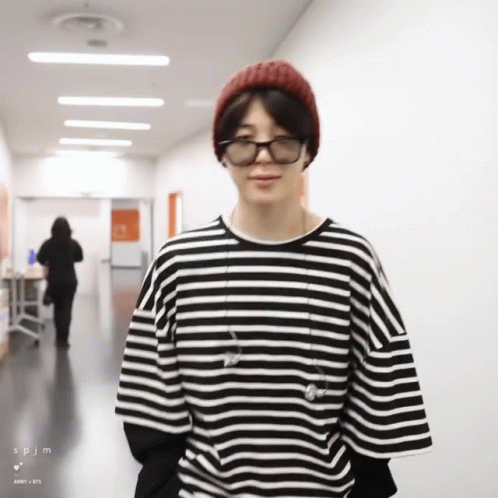 A Man Wearing A Striped Shirt And A Beanie Is Standing In A Hallway GIF